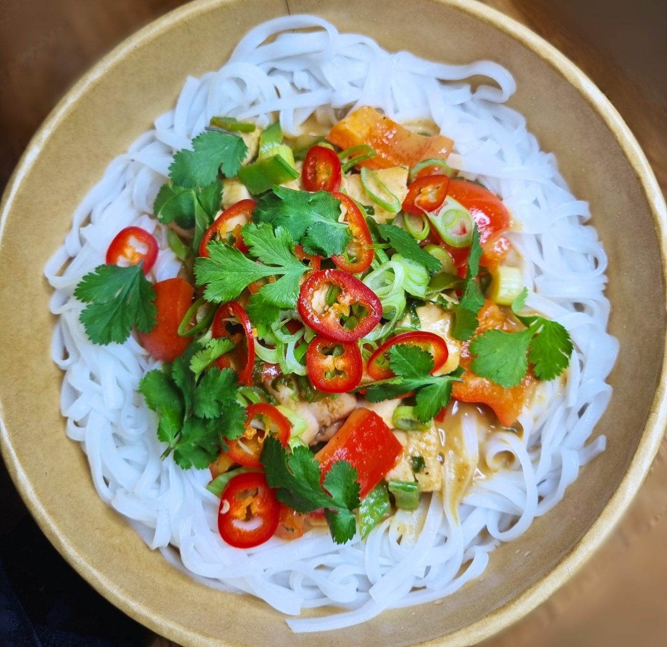 Pot of slow braised Jamaican beef curry with peppers and onions and white rice and baby peas, garnished with coriander. 